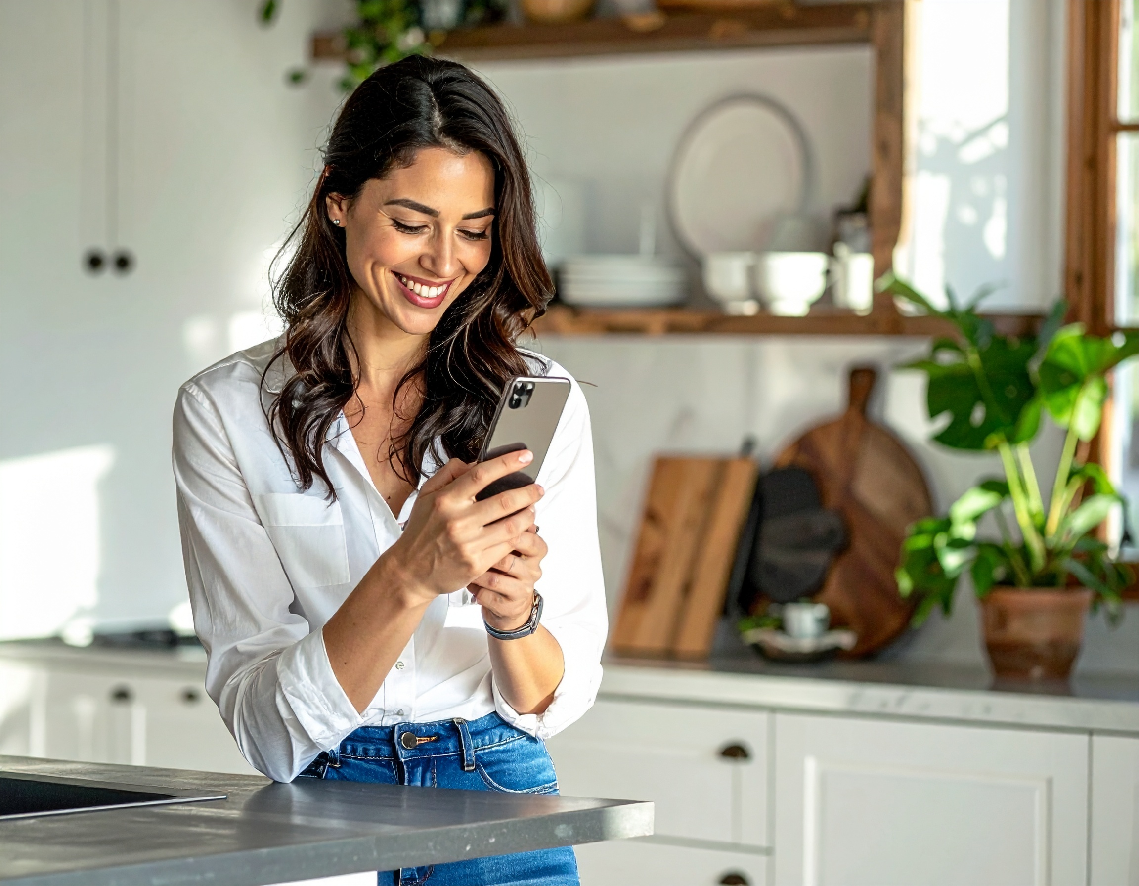 A woman looking at her phone in a bright kitchen.